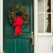 A green front door decorated with Christmas garland, a wreath, and a red ribbon.