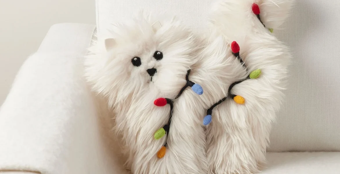 A fluffy white cat-shaped pillow wrapped in colorful Christmas lights on a white armchair.