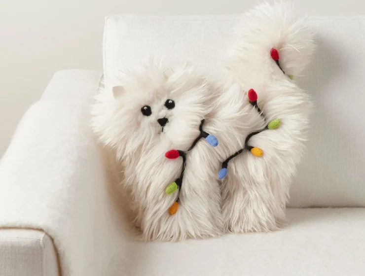 A fluffy white cat-shaped pillow wrapped in colorful Christmas lights on a white armchair.