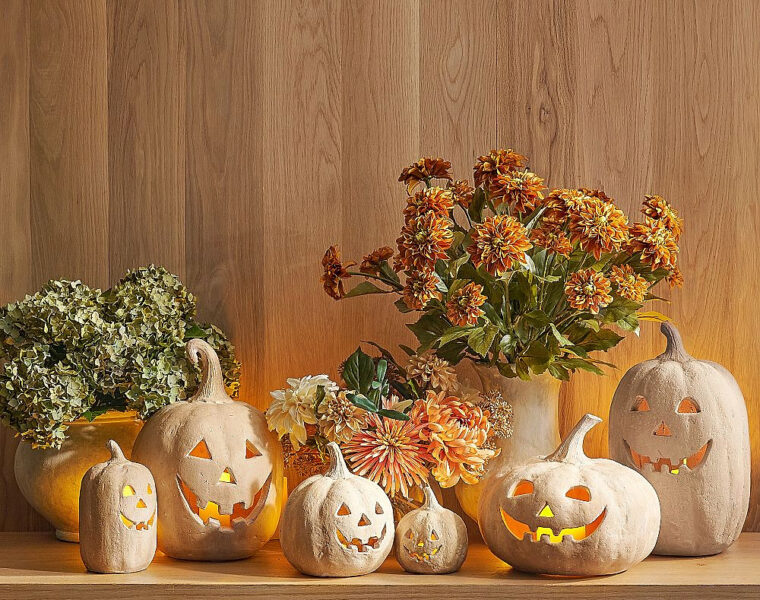 White jack-o’-lanterns and autumn flowers arranged on a wood-paneled table.