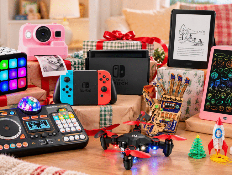 Tech gifts for kids under the Christmas tree, including a camera, Nintendo Switch, Kindle, drawing tablet, drone, and games