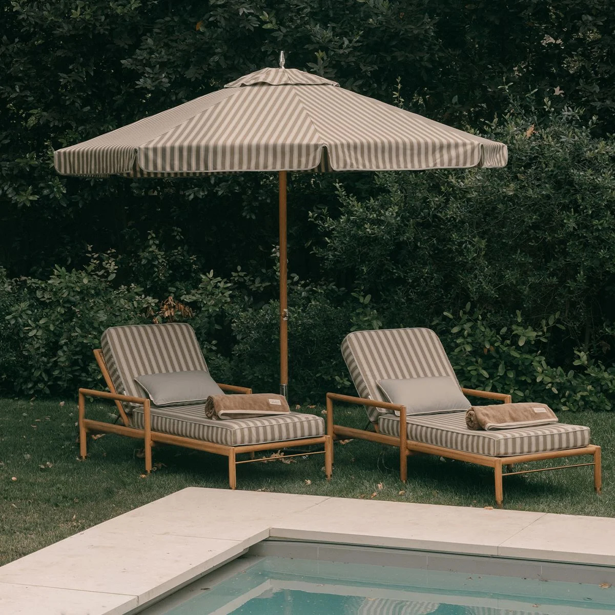 Striped patio umbrella and lounge chairs beside a pool.