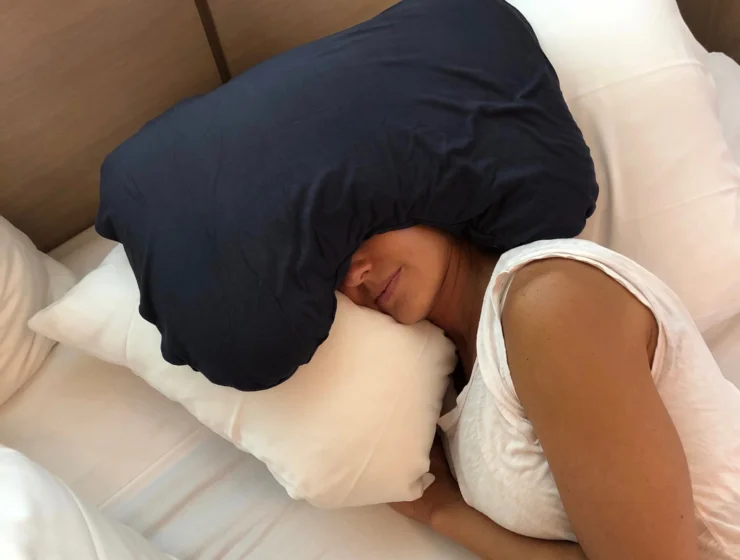 A person resting in bed with a navy Sleep Crown pillow over their forehead and eyes.