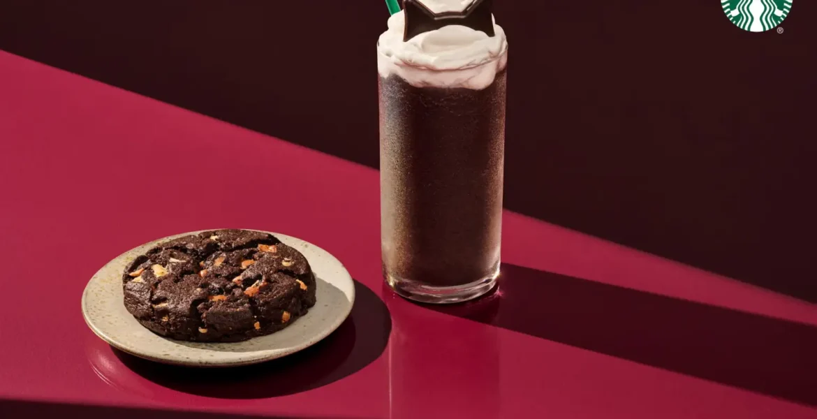 Starbucks Black Cat Frappuccino topped with whipped cream and chocolate cat ears beside a chocolate Halloween cookie.