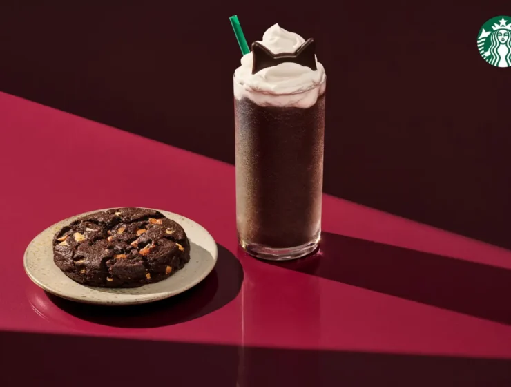 Starbucks Black Cat Frappuccino topped with whipped cream and chocolate cat ears beside a chocolate Halloween cookie.